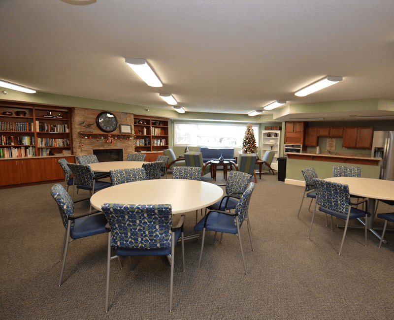 A spacious community room featuring round tables, chairs, and bookshelves.