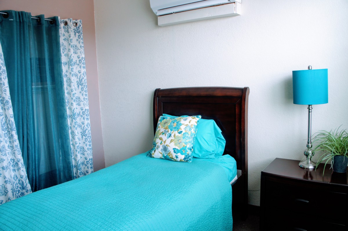 A cozy bedroom with a single bed and blue bedding, featuring an air conditioner above.