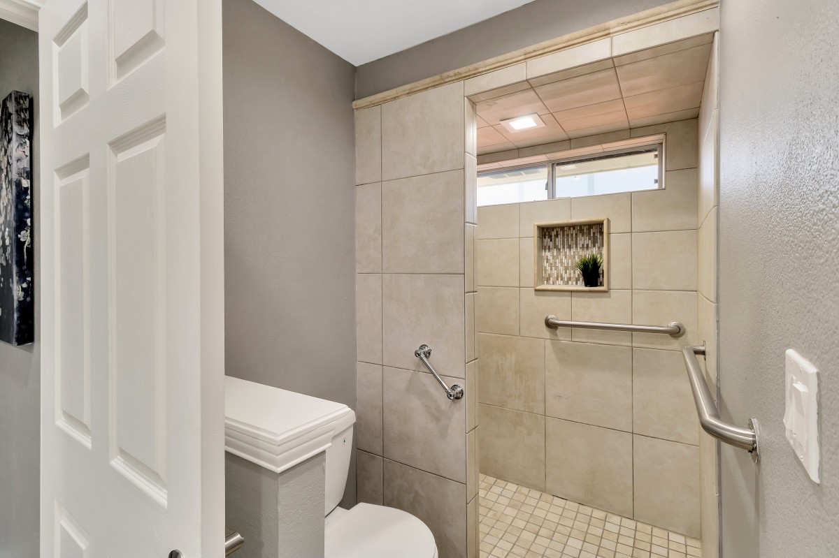 A modern bathroom featuring a walk-in shower with grab bars and neutral-toned tiles.