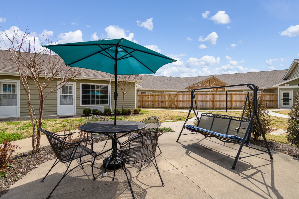 A cozy backyard patio featuring a table with chairs and an umbrella, alongside a comfortable swing.