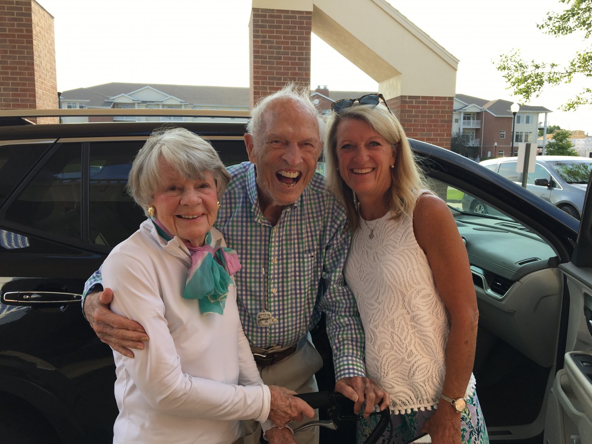 A cheerful group photo of three people standing together outside.