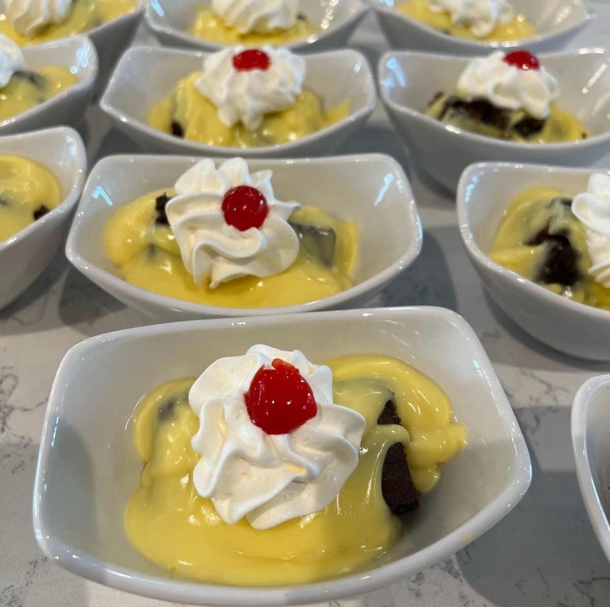 Delicious custard desserts topped with whipped cream and a cherry in elegant bowls.