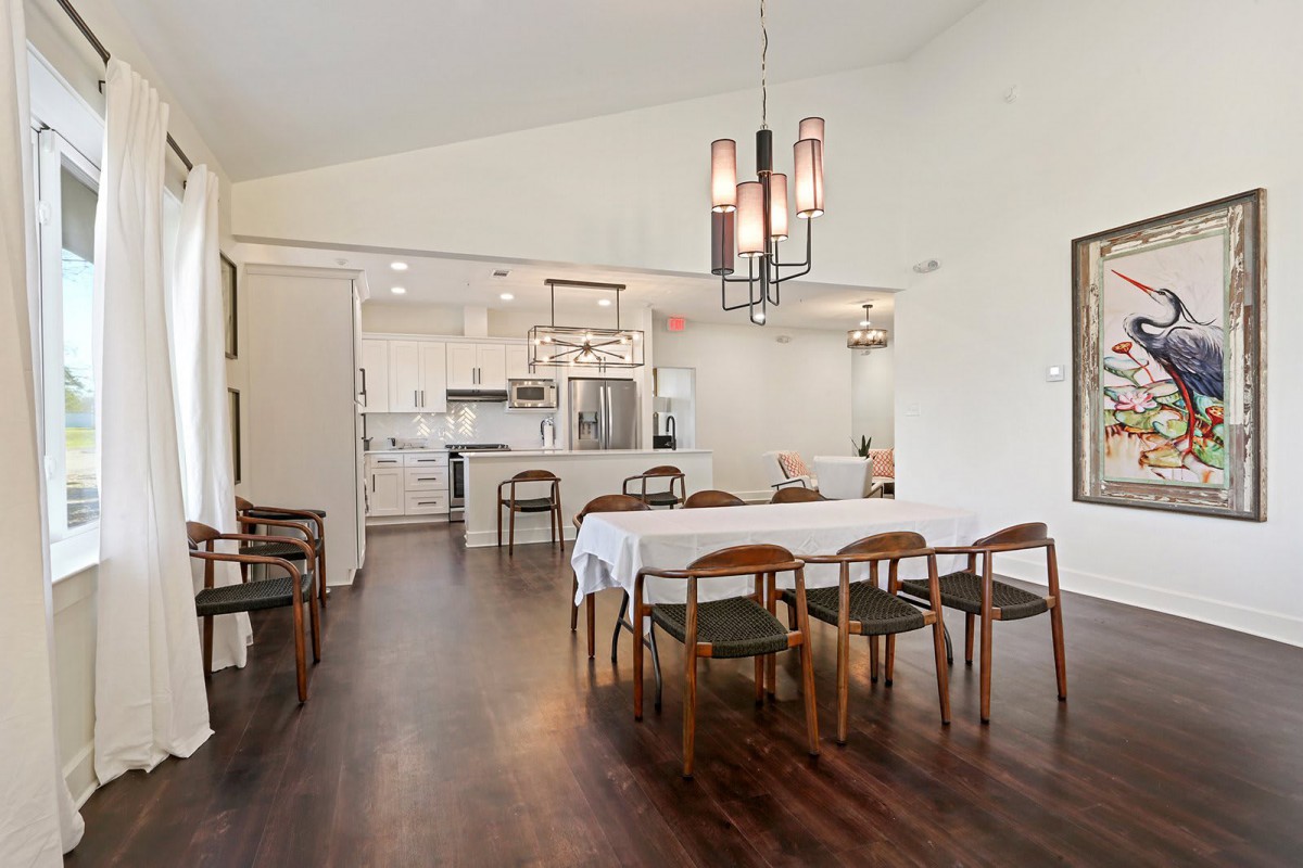 A modern open-concept dining and kitchen area featuring wood flooring, a contemporary chandelier, and stylish furniture.