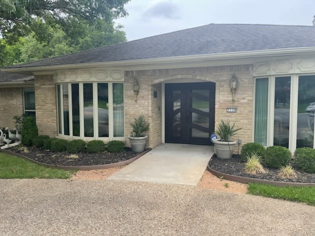 A brick house entrance with large windows and potted plants.