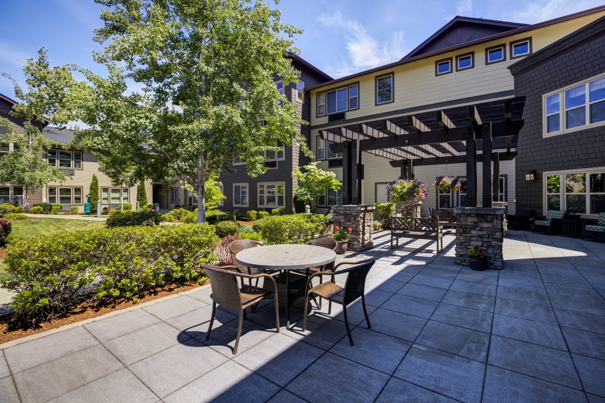 A cozy outdoor patio with tables and chairs surrounded by lush greenery and adjacent to a building.
