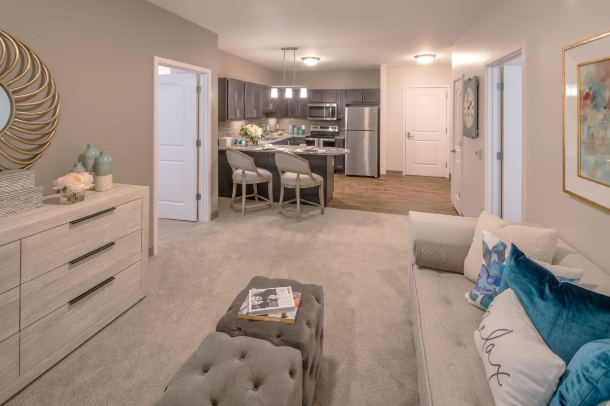 A modern open-concept apartment living area with stylish furniture and a view into the kitchen.