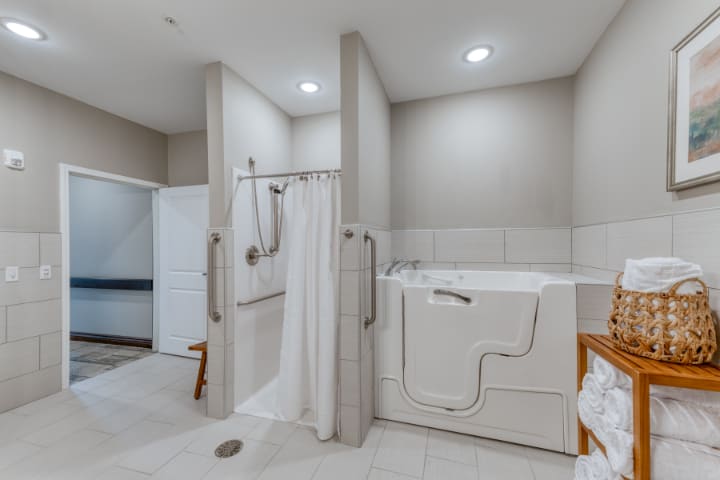 A modern, accessible bathroom featuring a walk-in shower and bathtub with safety grab bars.