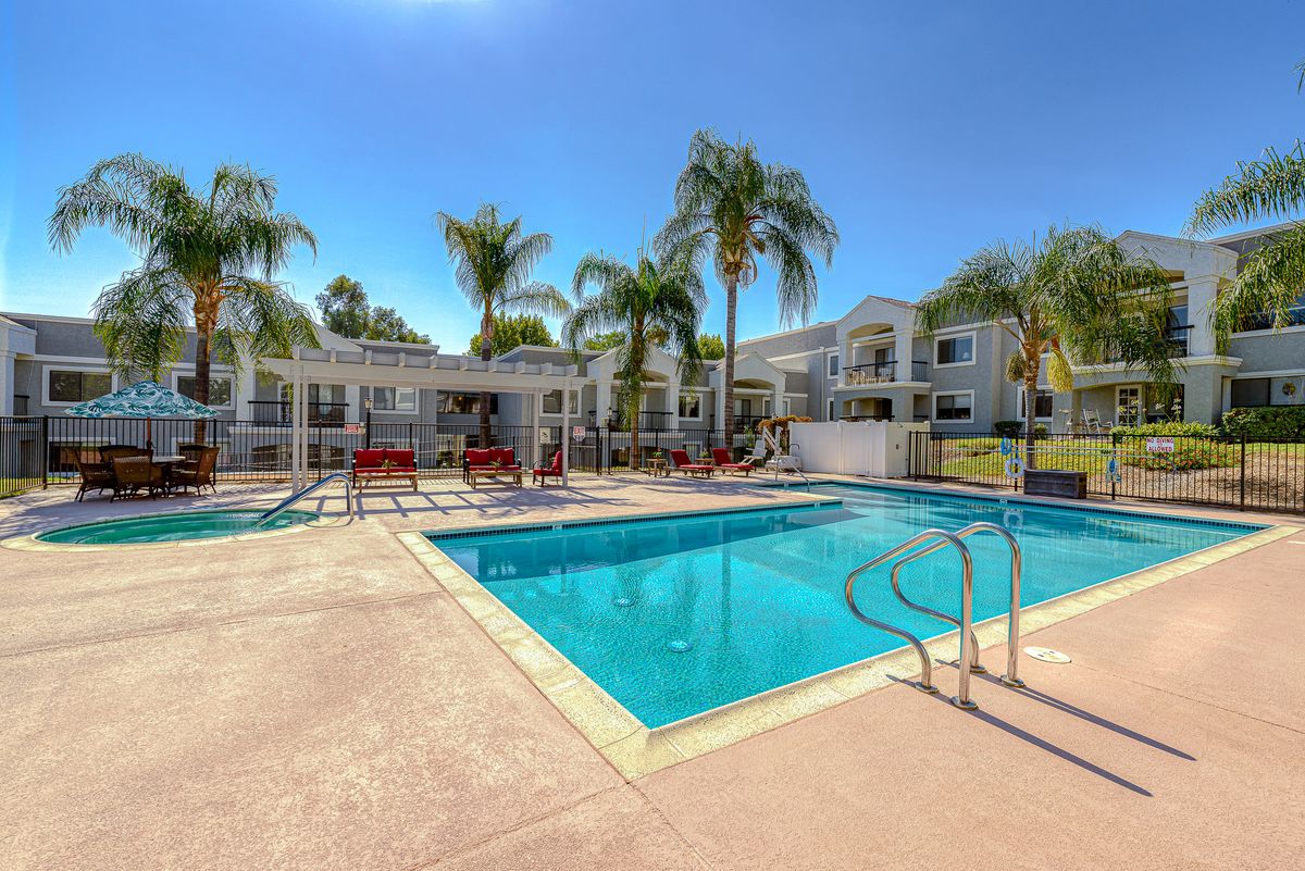 A sunny day at a residential apartment complex featuring a large outdoor swimming pool surrounded by palm trees.