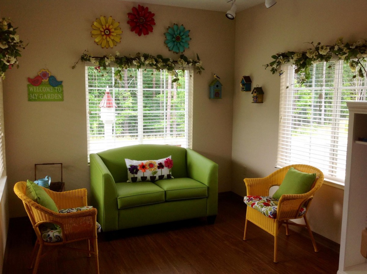 A cozy living room with a green couch and yellow chairs, featuring colorful decorations and ample natural light from the windows.