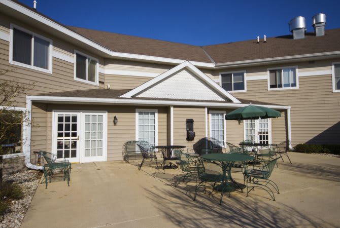 A two-story house with an outdoor patio area featuring tables and chairs under a clear blue sky.