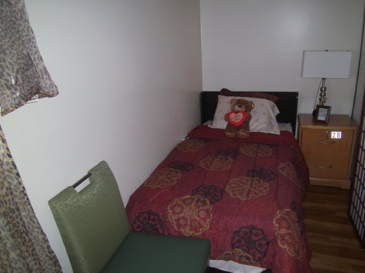 A small, cozy bedroom with a single bed and a teddy bear on the pillow.