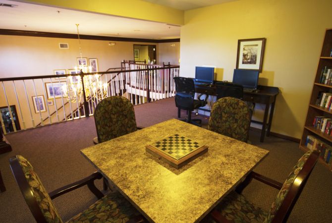 A cozy seating area with a chessboard on a table, surrounded by chairs and overlooking a railing with work desks nearby.