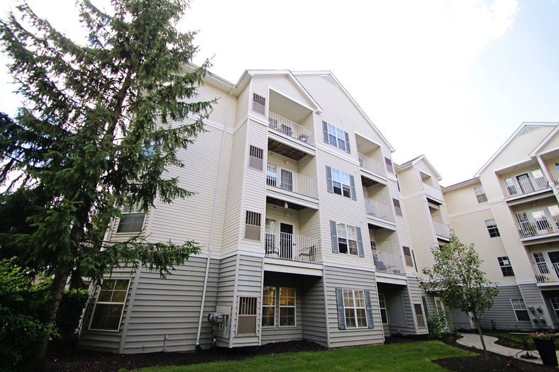 A multi-story apartment building with balconies, surrounded by trees and grass.