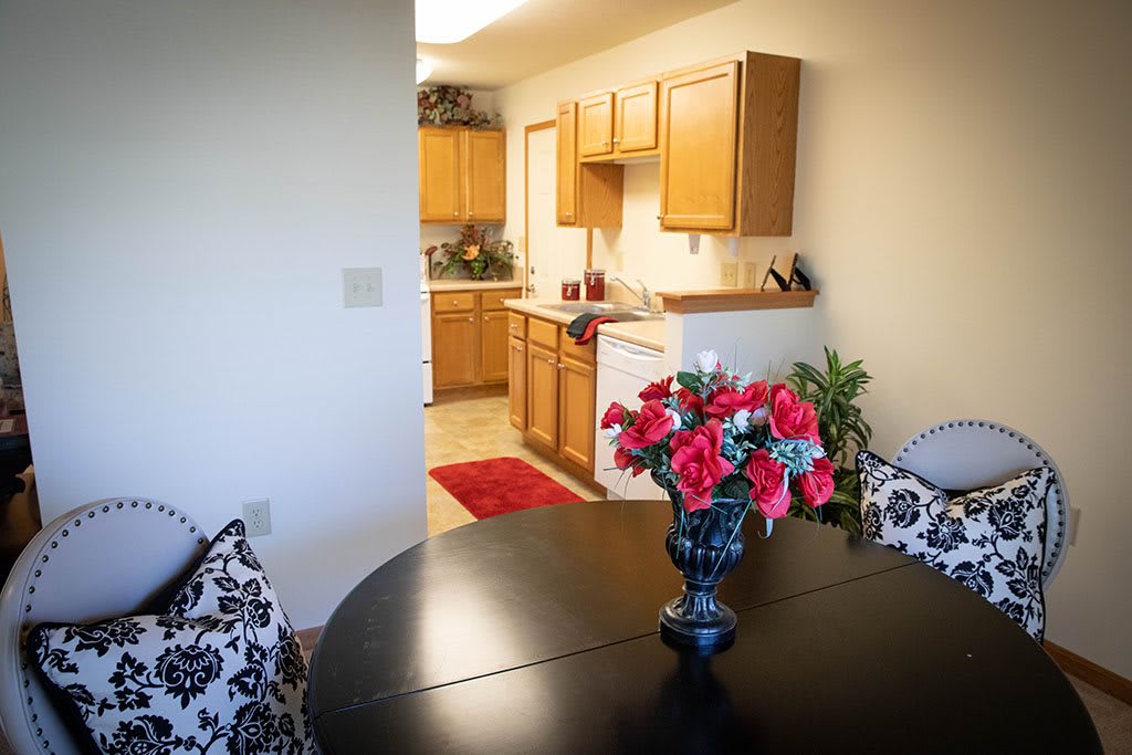 A cozy dining area with a black table and floral centerpiece, leading into a warm kitchen space.