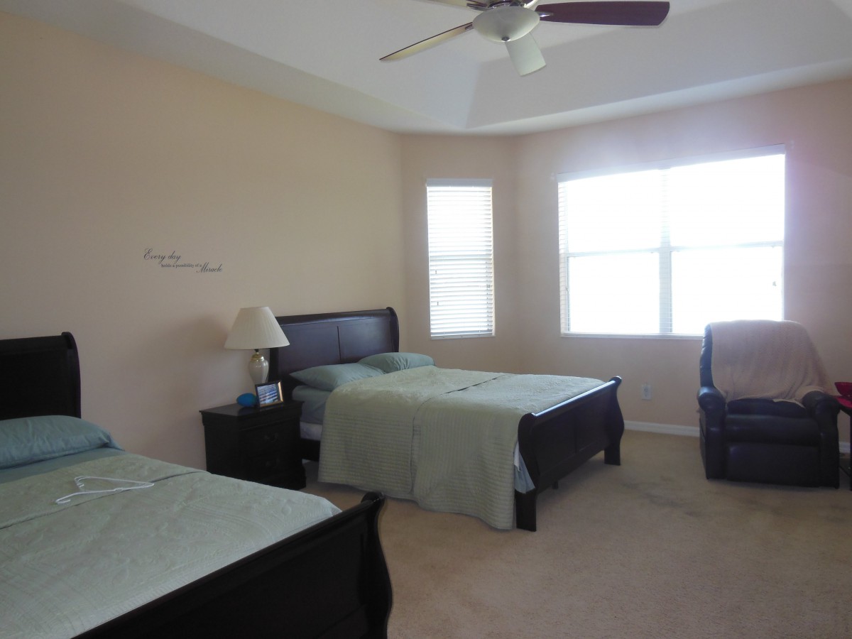 A spacious bedroom with two twin beds, a nightstand with a lamp, and large windows that let in natural light.