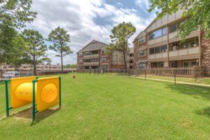 A grassy outdoor area in an apartment complex with surrounding buildings and trees.