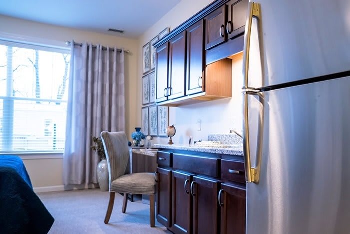 A cozy kitchen interior with dark wood cabinets, a fridge, and a window with curtains.