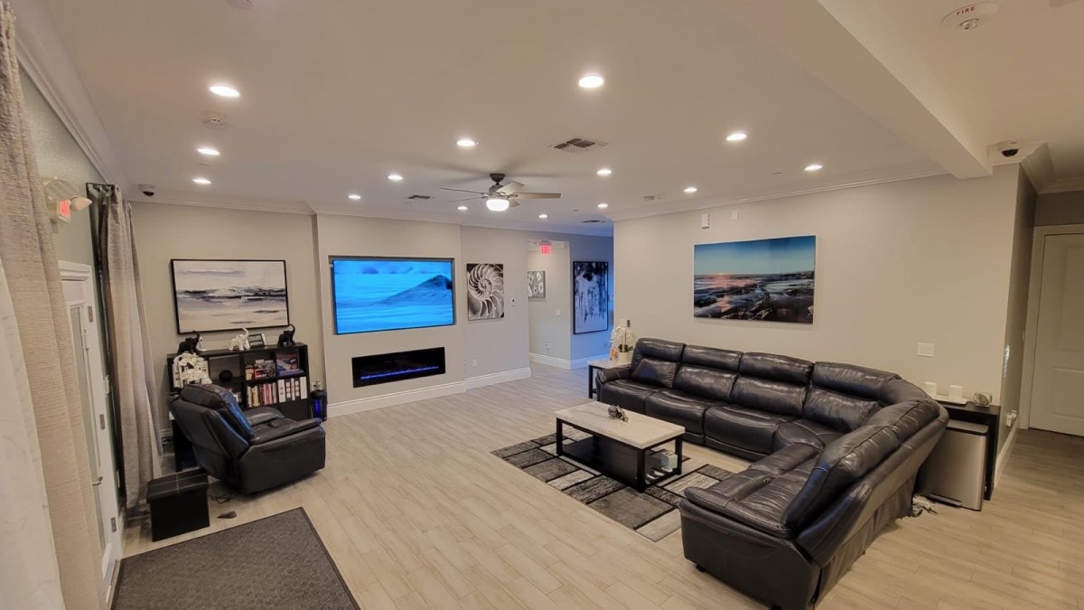 A modern living room featuring a large sectional sofa, a flat-screen TV, wall art, and recessed lighting.