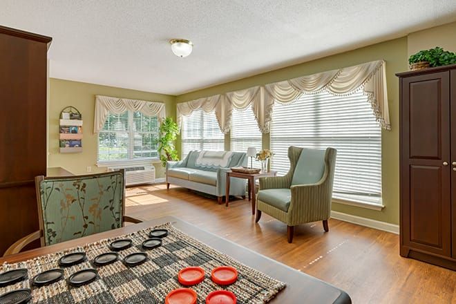 A cozy living room with large windows, comfortable seating, and a checkers game set up on the table.