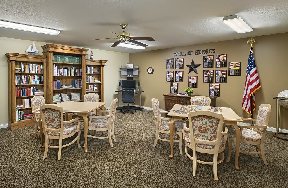 A cozy room featuring tables and chairs, a bookshelf filled with books, and decorative items on the wall.