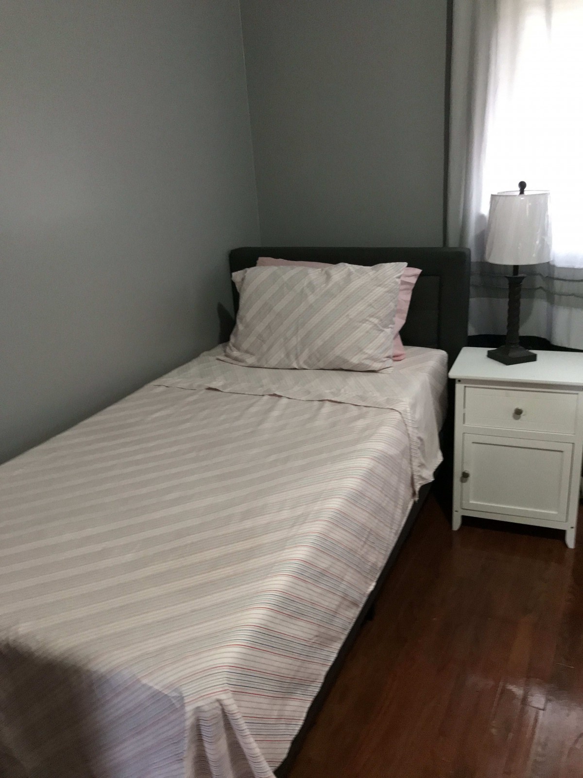 A minimalist bedroom with a single bed and a nightstand featuring a lamp.