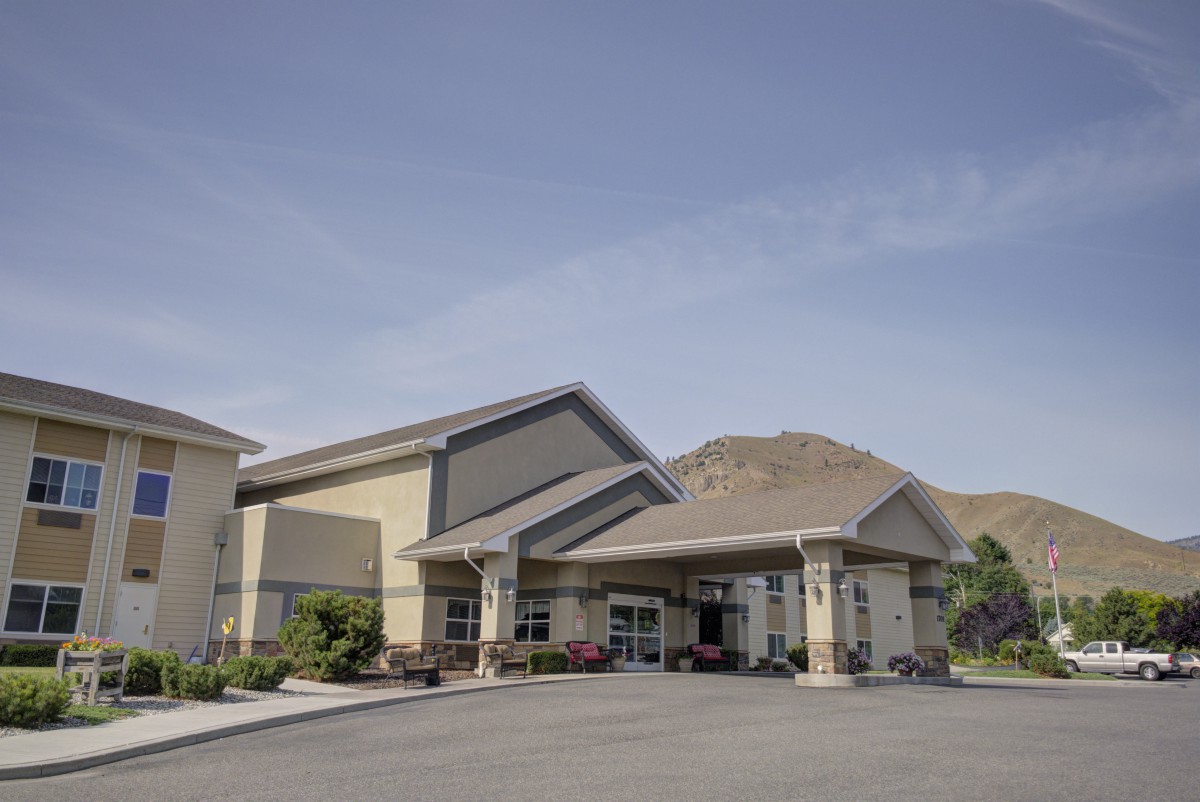 A modern building with a driveway and mountain in the background on a clear day.