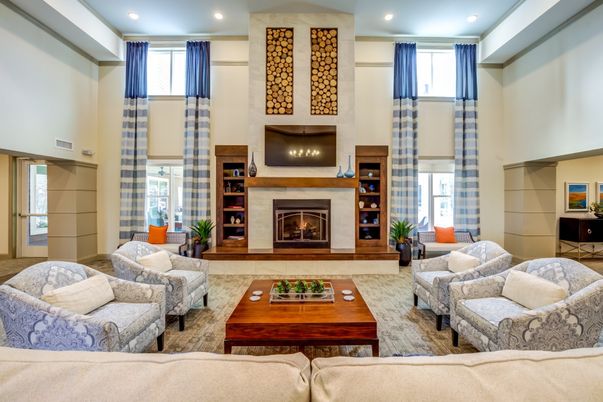 A spacious and elegantly designed living room featuring a central fireplace, comfortable sofas, and large windows with blue curtains.