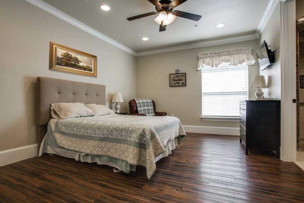 A cozy bedroom with a neatly made bed, hardwood floors, and a ceiling fan.