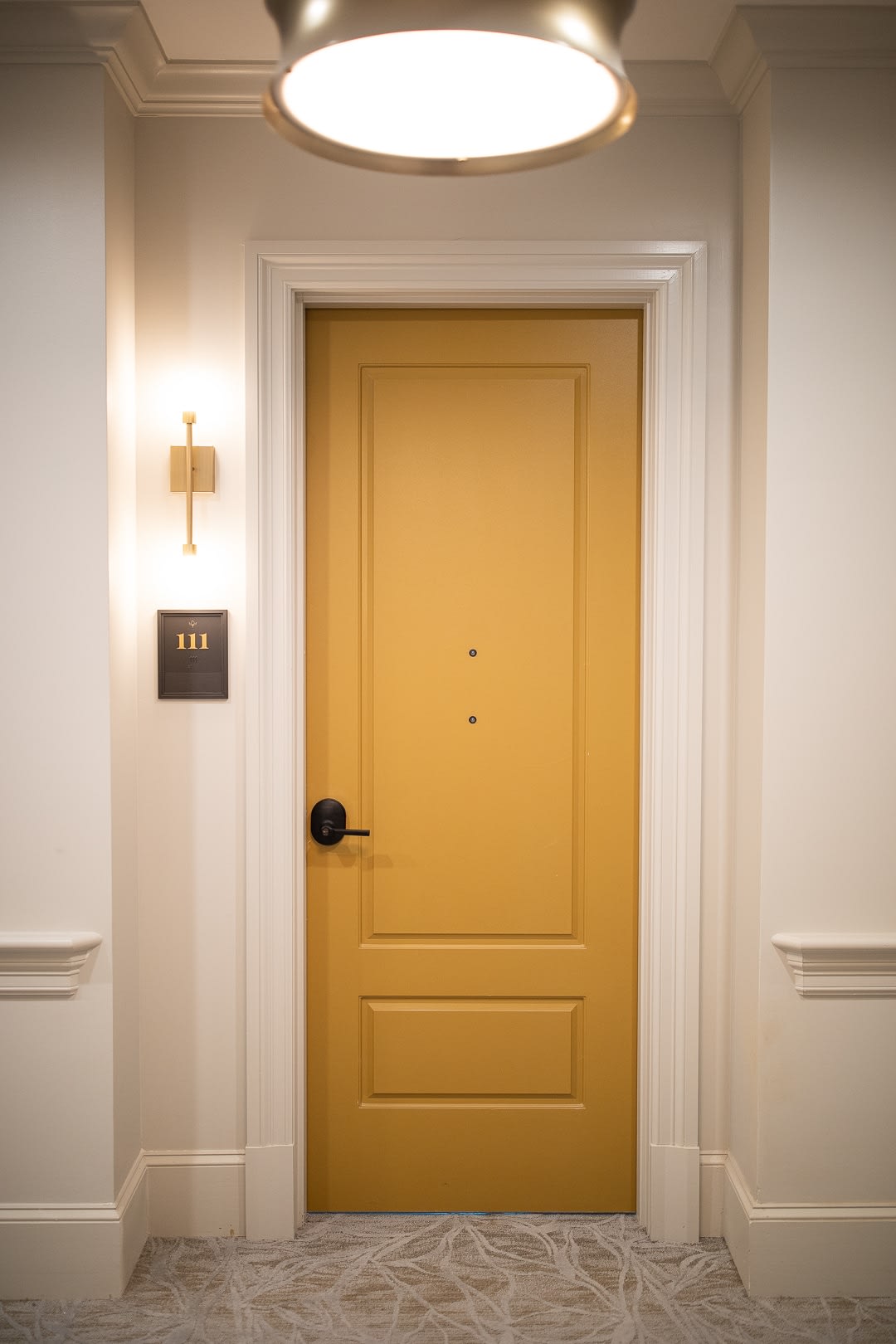A luxurious hotel room door with an elegant light fixture in a hallway.
