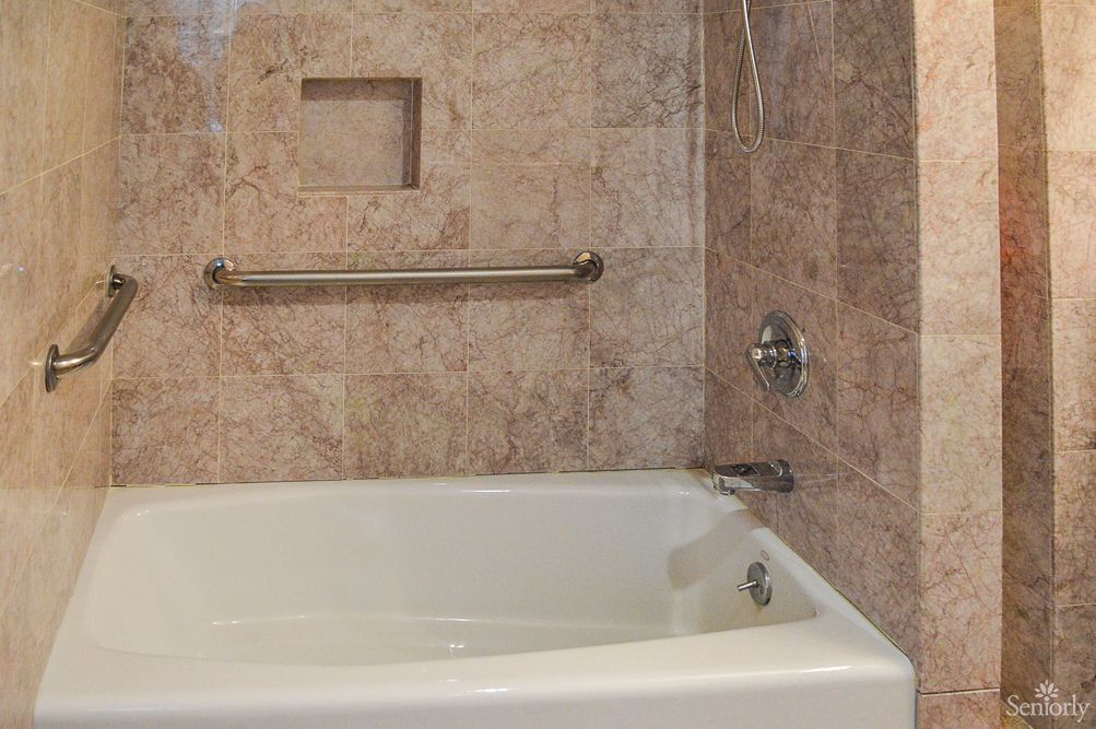 A bathroom featuring a bathtub with tiled walls and a grab bar.