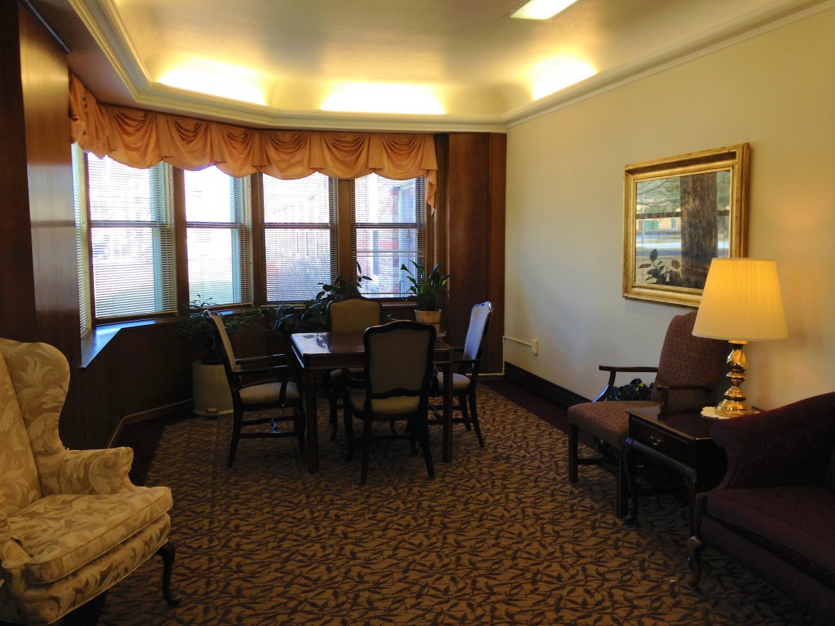 A cozy living room with a table and chairs set, surrounded by large windows and warm lighting.