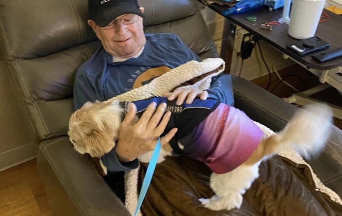 A man sitting in a chair holding a dog on his lap indoors.