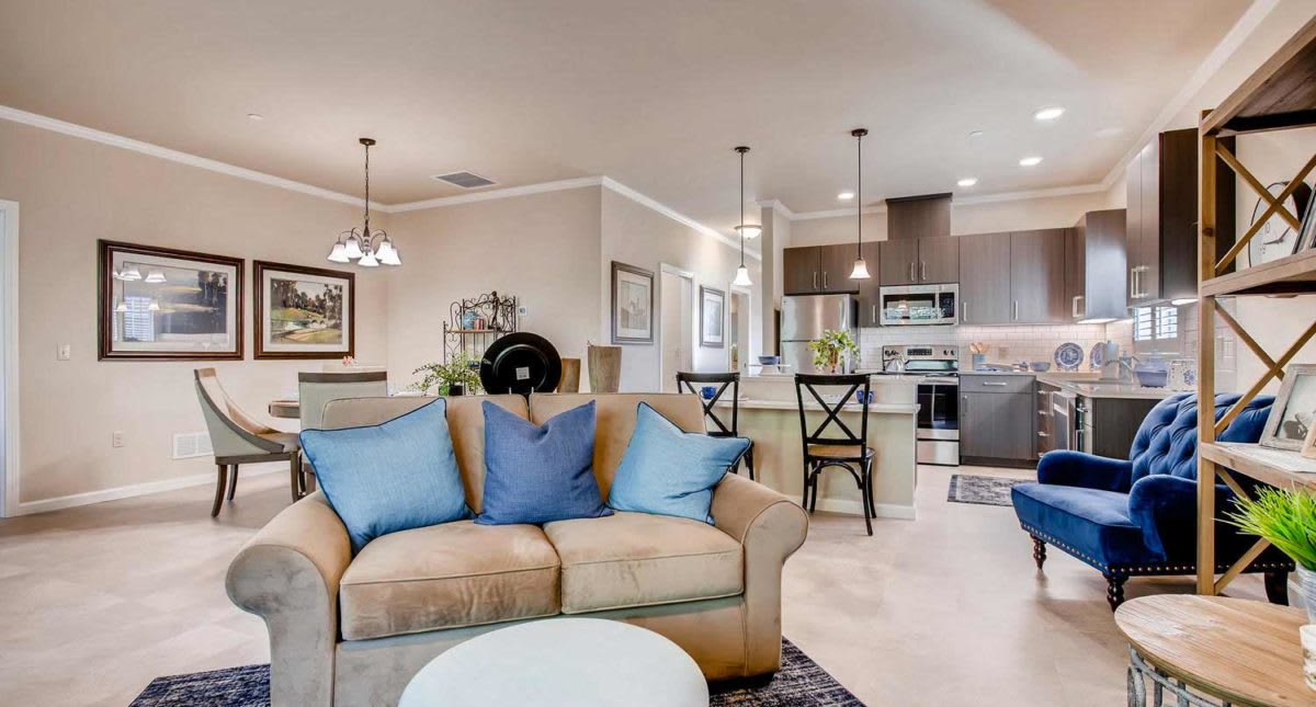 A modern open-concept living area with a comfortable sofa featuring blue pillows, a kitchen island with barstools, and elegant pendant lighting.