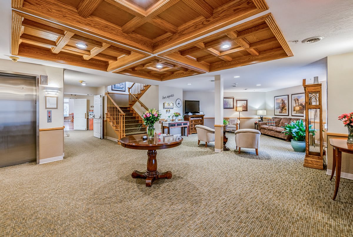 A spacious and elegantly designed lobby featuring comfortable seating, a wooden ceiling, and a central table with floral arrangements.