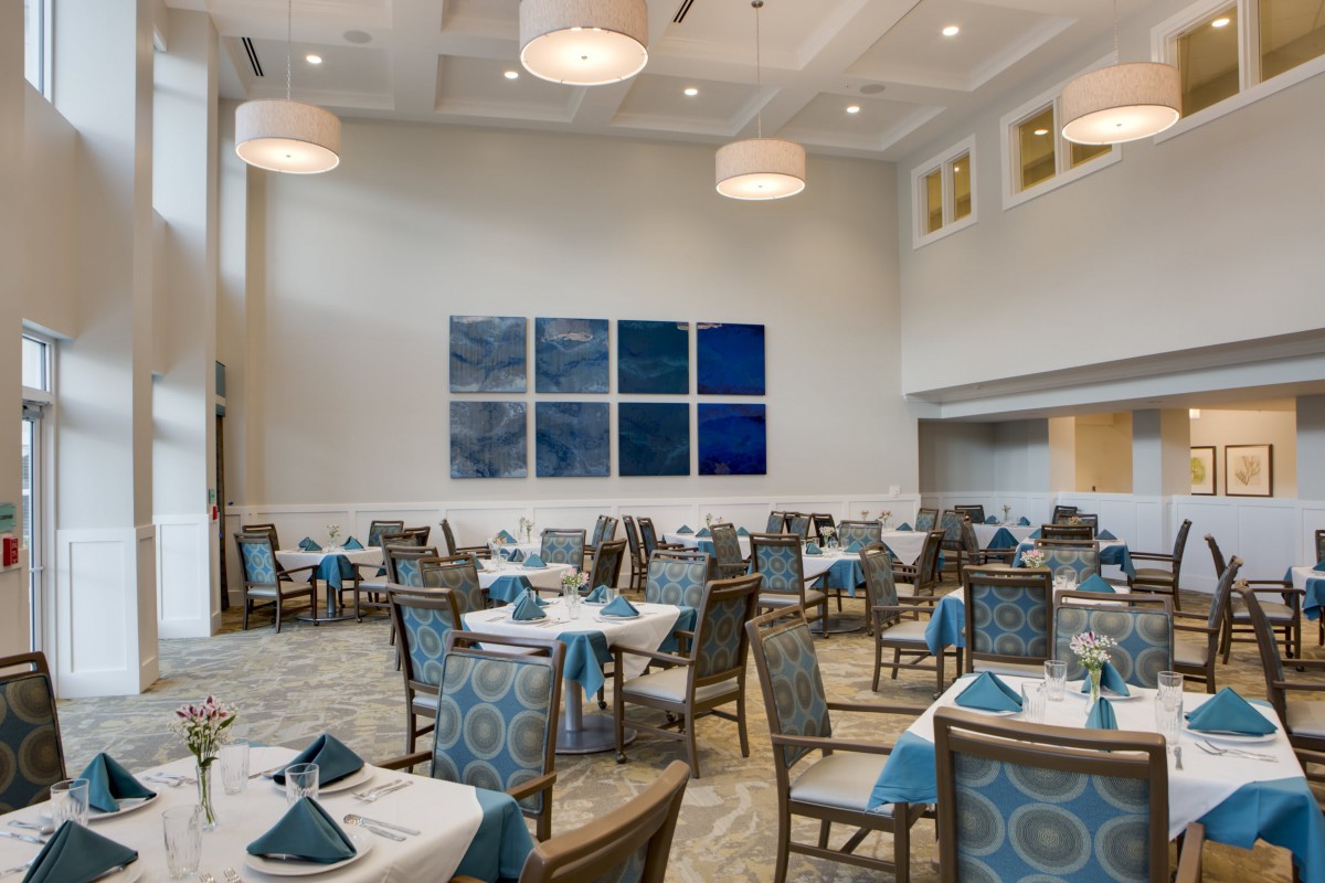 A modern restaurant dining area with neatly arranged tables and chairs, featuring elegant decor and artwork on the wall.