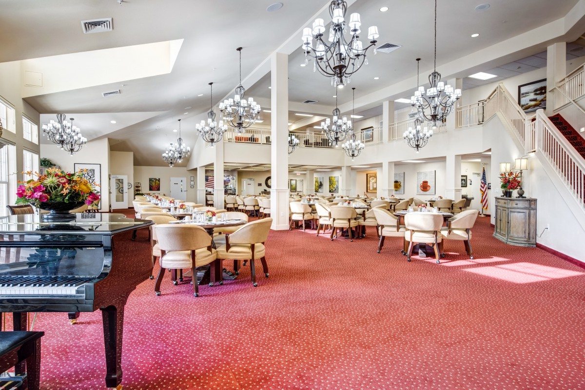 An elegant dining room with plush carpet, chandeliers, and a grand piano.