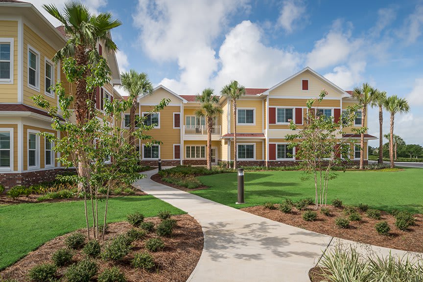 A sunny residential complex with palm trees and a well-maintained lawn.