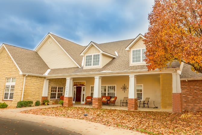 A suburban house with a front porch surrounded by autumn leaves and trees.