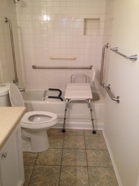 An accessible bathroom with grab bars, a shower chair, and tiled flooring.