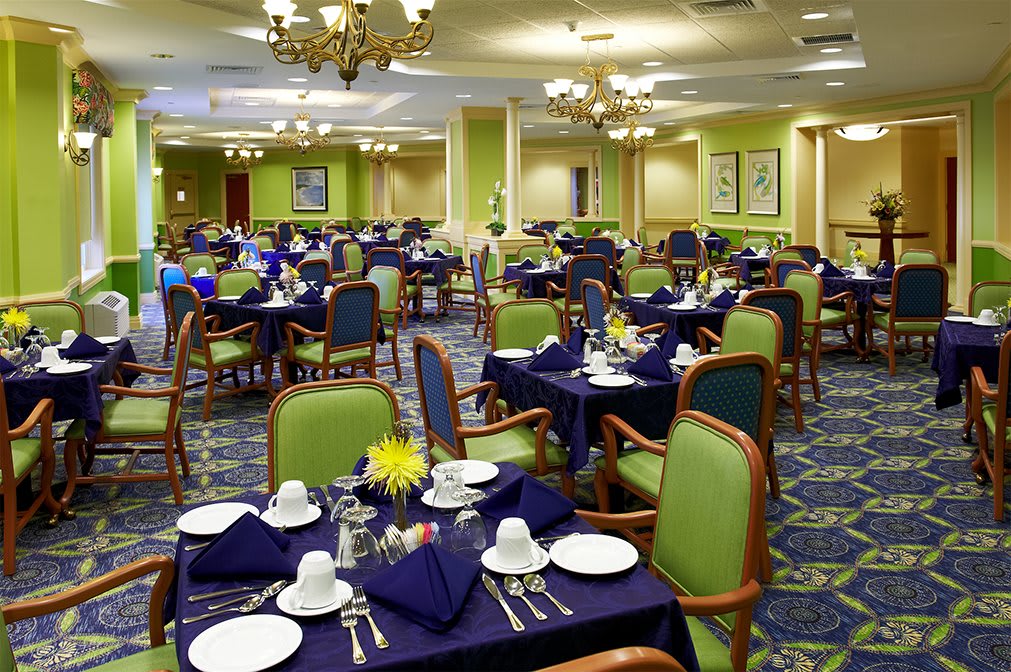 A spacious dining room with neatly arranged tables and chairs, featuring elegant place settings and chandeliers.