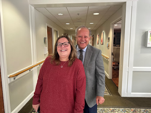 Two friends posing together in a hallway, both smiling warmly.