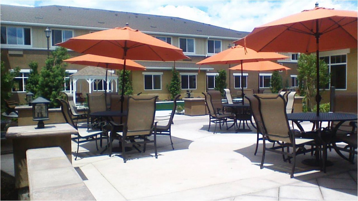 A patio area with tables, chairs, and orange umbrellas in front of a residential building.