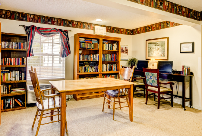 A cozy home office with a wooden table, chairs, and a bookshelf filled with books.