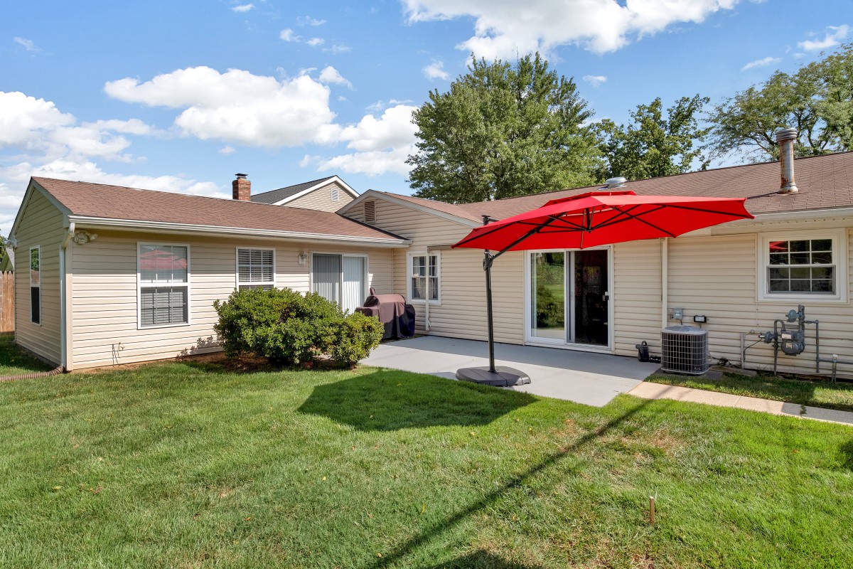 A sunny backyard featuring a patio with a red umbrella and well-maintained lawn.