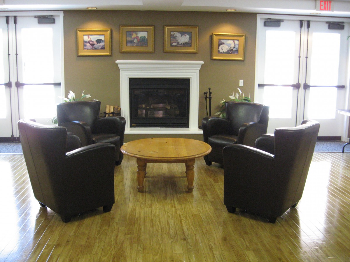 A cozy living room with a fireplace, surrounded by leather armchairs and a wooden table.