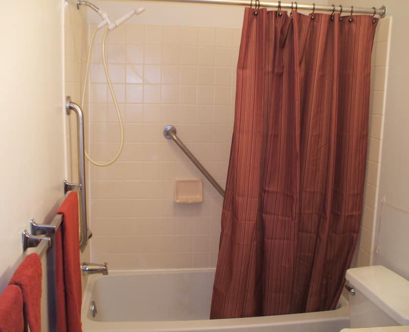 A bathroom featuring a bathtub with a brown shower curtain and a safety grab bar.