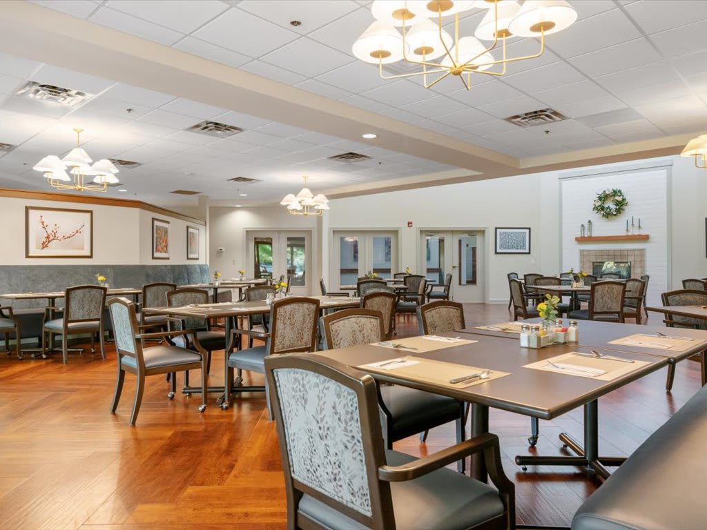 A spacious dining room with neatly arranged tables and chairs, illuminated by elegant chandeliers.