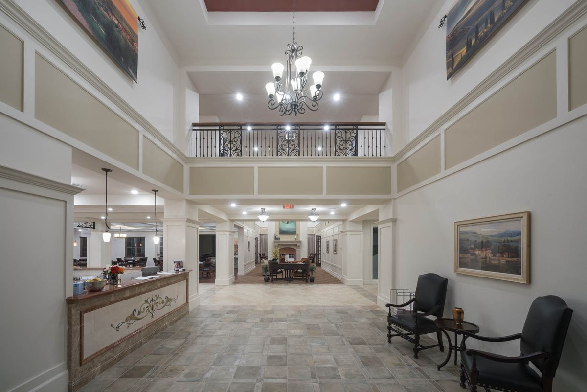 A spacious and well-lit lobby with a central chandelier, reception desk, and seating area.