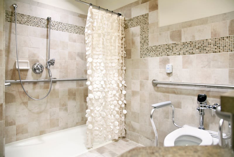 An accessible bathroom with tiled walls, a shower area with handrails, and a decorative shower curtain.