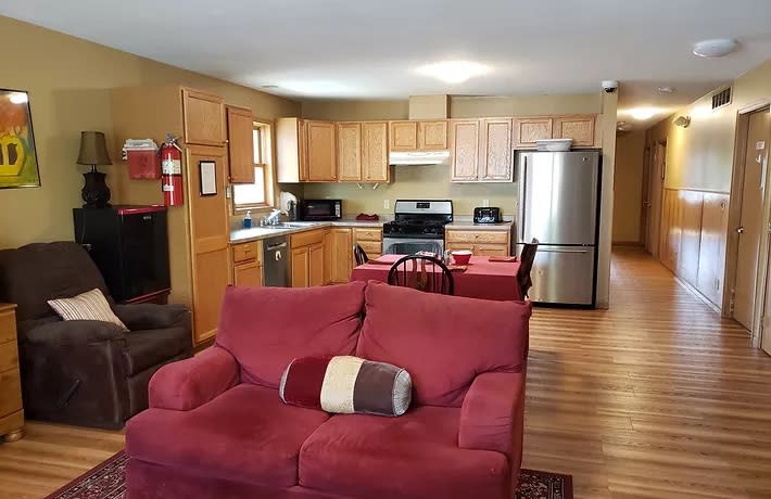 An open floor plan combining a living room and kitchen, featuring a red sofa, wooden cabinets, and modern appliances.